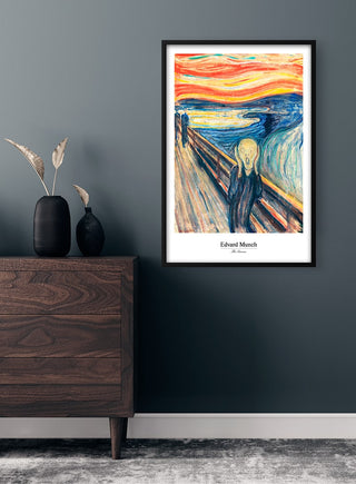 Framed Edvard Munch - The Scream poster hanging on a dark wall above a wooden dresser in a modern room.
