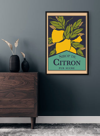 Framed Sirop De Citron Plakat poster with yellow lemons and green leaves on a wall above a wooden dresser.
