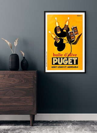 Vintage Puget olive oil poster with bottles and black olives on a yellow background, framed on a dark wall.