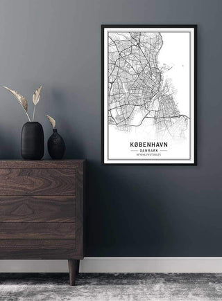 Framed map poster of Copenhagen hanging on a dark wall above a wooden cabinet with vases.