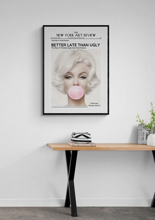 Framed Marilyn Monroe - Art Review Plakat featuring her blowing pink bubble gum, displayed above a wooden desk.