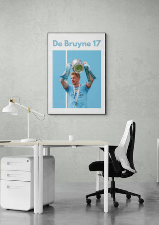 De Bruyne Man City Football Poster featuring a player holding a trophy, hung above an office desk.