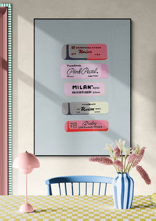 Framed art print featuring vintage erasers displayed vertically, hung above a table with flowers in a vase.