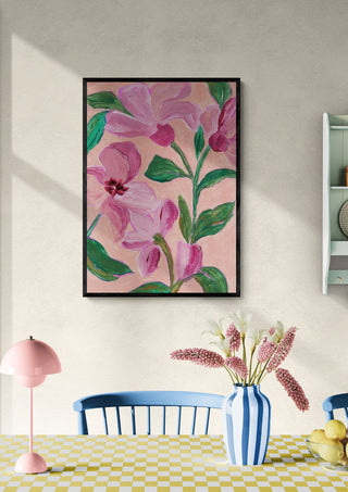 Framed artwork of pink flowers with bold green leaves hanging on a wall above a dining table.