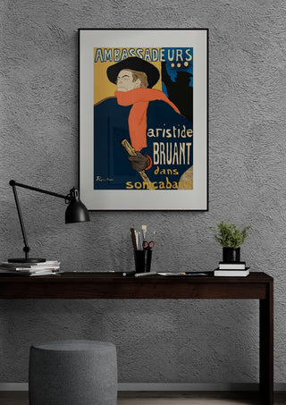 Poster of Aristide Bruant Dans Son Cabaret by Lautrec framed above a modern desk against a textured wall.