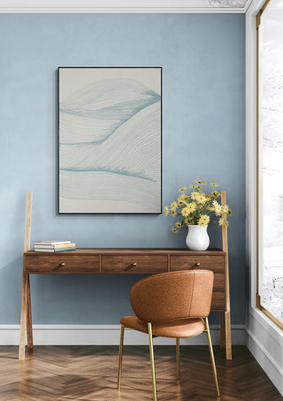 Framed "Ocean in lines 02" artwork on a blue wall above a wooden desk with flowers and a brown chair.