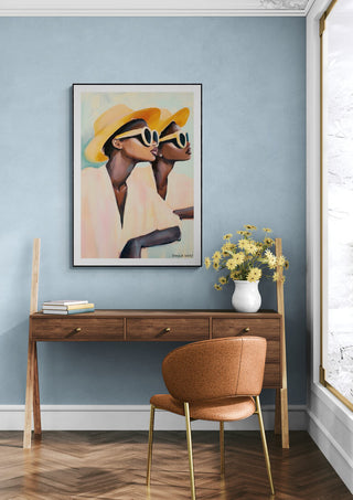 Framed "Hey Look" by David Wolf on blue wall above wooden desk with chair and vase of yellow flowers.