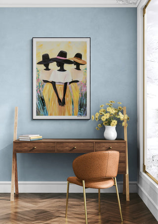 Framed "Fields of Love" by David Wolf hanging above a wooden desk with flowers in a vase.