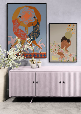 Two colorful Sisterhood - Arty Guava art prints in black frames displayed above a pink sideboard.