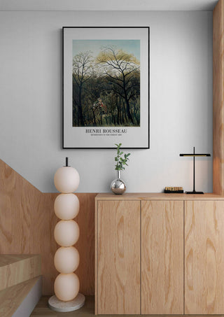 Framed "Rendezvous In The Forest" by Henri Rousseau displayed above a modern wooden cabinet in a minimalist room.