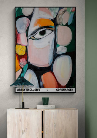 Abstract painting with colorful shapes and a central eye, displayed above a light wooden cabinet.