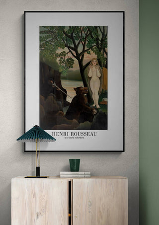 Framed Mauvaise Surprise by Henri Rousseau displayed above a light wood cabinet in a modern room.