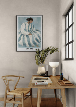 Framed "Elegance in the Garden - Elara Monet" art above a minimalist desk with decor and a wooden chair.